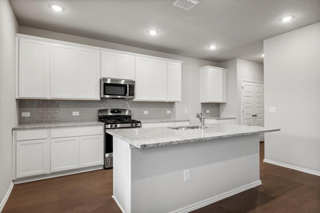 12212 Dillon Fls Drive Austin, TX 78747 - Photo 10 of 40 Kitchen with stainless steel appliances, backsplash, light stone counters, white cabinets, and a kitchen island with sink