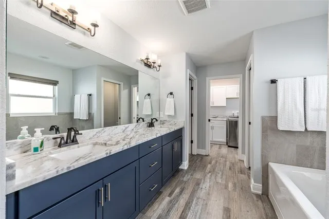 a spacious bathroom with a granite countertop double vanity sink a mirror a bathtub and