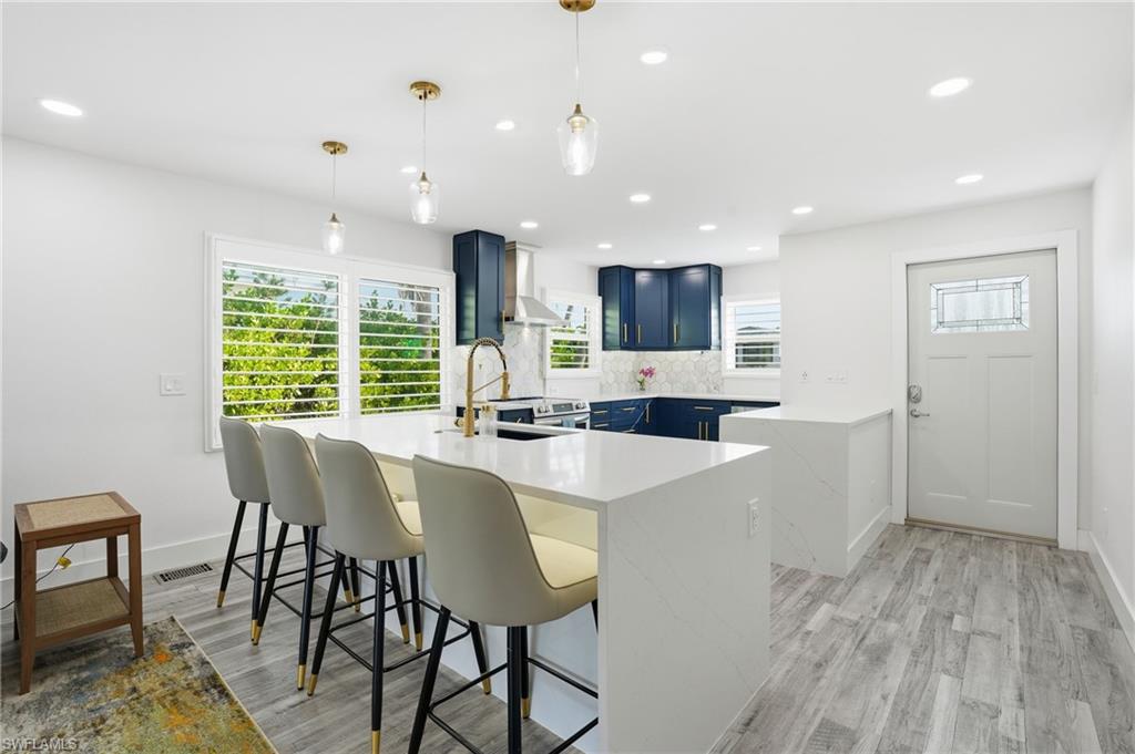 270 Dundee Road Fort Myers Beach, FL 33931 - Photo 14 of 48 Kitchen featuring a peninsula, blue cabinetry, a breakfast bar, light stone countertops, and hanging light fixtures - Virtually Edited Image