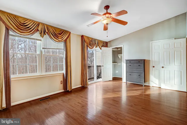 an empty room with wooden floor fan and windows