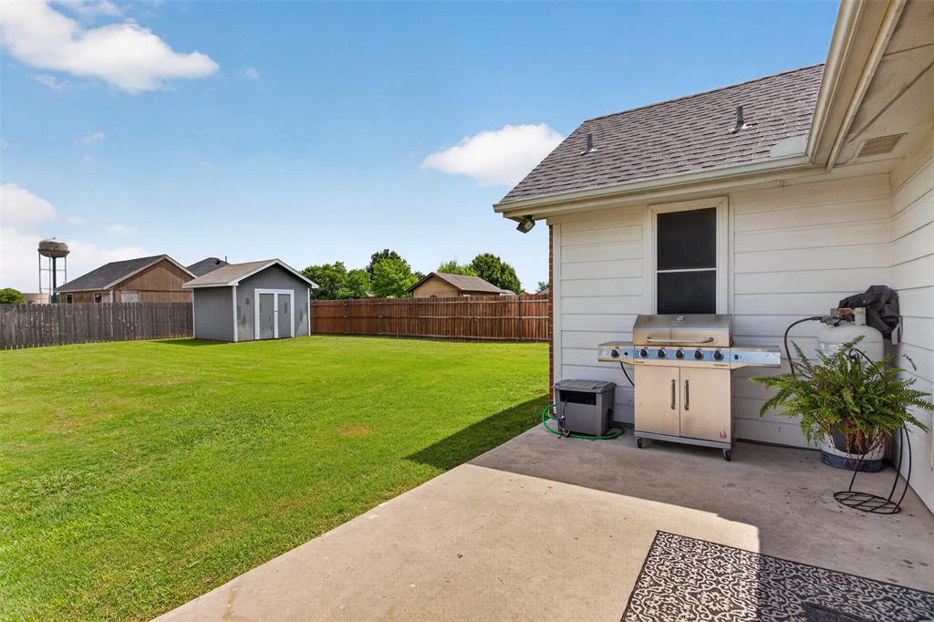 100 Radecke Road Krum, TX 76249 - Photo 27 of 29 Expansive backyard featuring a large concrete patio, wood privacy fencing, and a separate storage shed