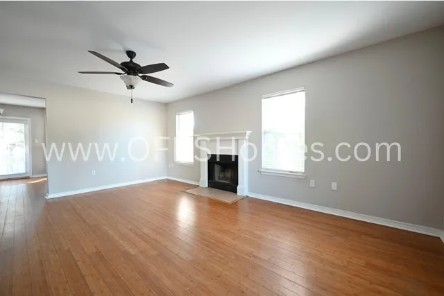 an empty room with wooden floor fireplace and windows