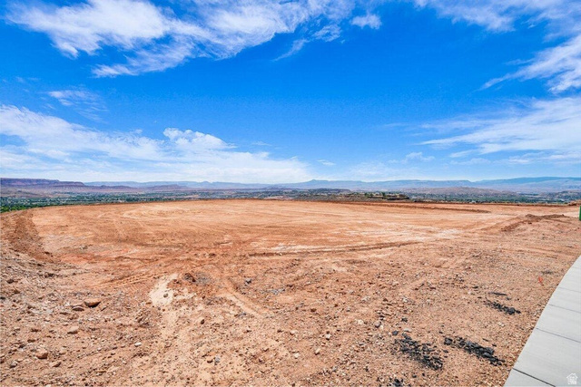 Undisclosed Address St. George, UT 84770 - Photo 9 of 11 Expansive undeveloped land featuring a paved walkway border, a wide-open terrain, distant urban elements, and a mountainous horizon under a broad sky