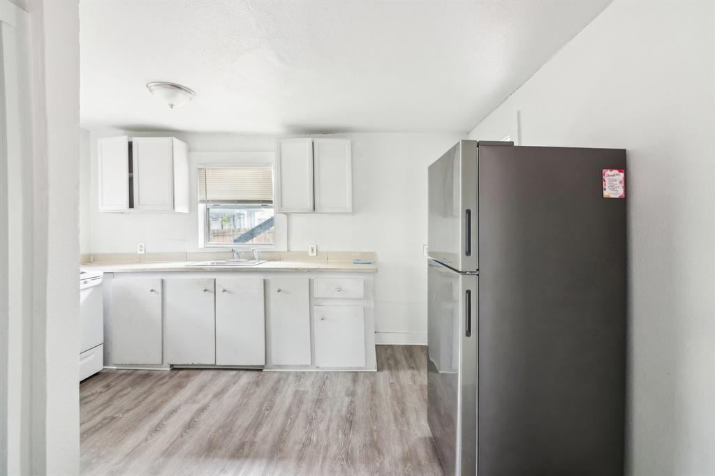 1906 Grainger Street Fort Worth, TX 76110 - Photo 6 of 38 Kitchen with stainless steel refrigerator, sink, white cabinets, and light hardwood / wood-style floors