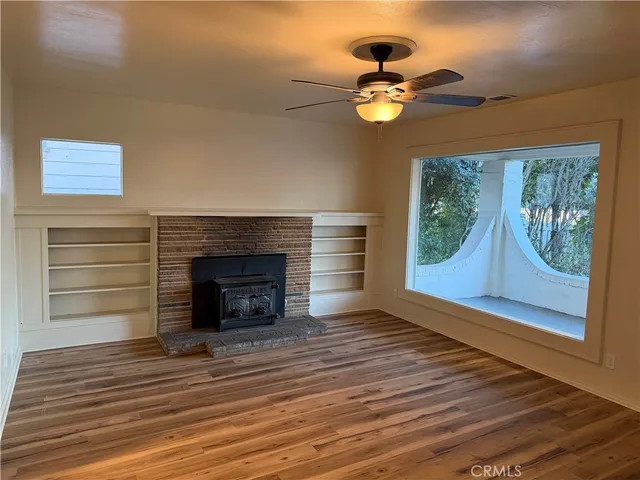 a view of an empty room with wooden floor fireplace and a window