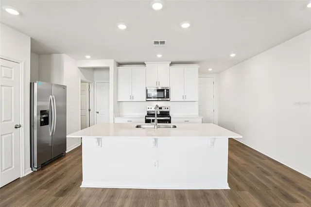 a large kitchen with stainless steel appliances granite countertop a white stove top oven a refrigerator a sink and a refrigerator