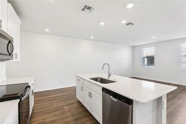 a kitchen with a sink dishwasher and white cabinets with wooden floor