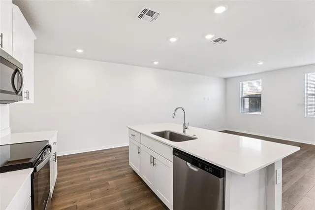 a kitchen with a sink dishwasher and white cabinets with wooden floor
