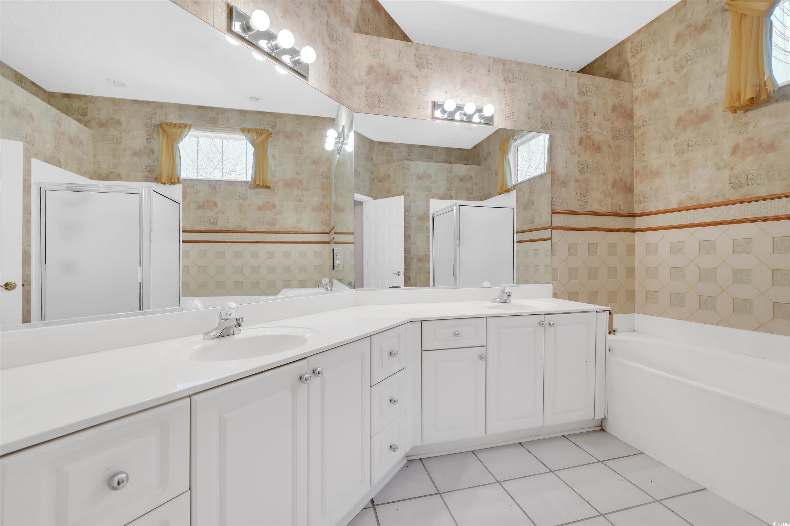 9350 Pinckney Lane Murrells Inlet, SC 29576 - Photo 17 of 40 Bathroom featuring healthy amount of natural light, light tile patterned floors, double vanity, a garden tub, and wallpapered walls