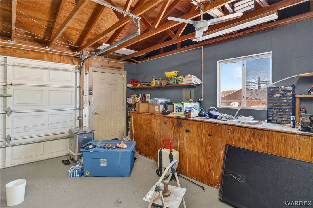 784 Pegasus Ranch Road Bullhead City, AZ 86429 - Photo 55 of 100 Spacious garage with exposed wood beam ceiling, concrete flooring, a paneled garage door, and a built-in workbench with storage