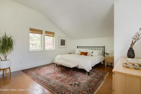 a bed sitting in a bedroom next to a window with a lamp on table and chair