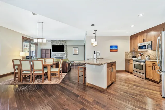 a kitchen with stainless steel appliances kitchen island granite countertop a stove top oven a sink a dining table and chairs with wooden floor