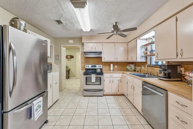 a kitchen with stainless steel appliances granite countertop a refrigerator a sink dishwasher a stove and white cabinets with wooden floor