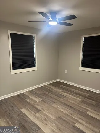 a view of an empty room with wooden floor and a ceiling fan