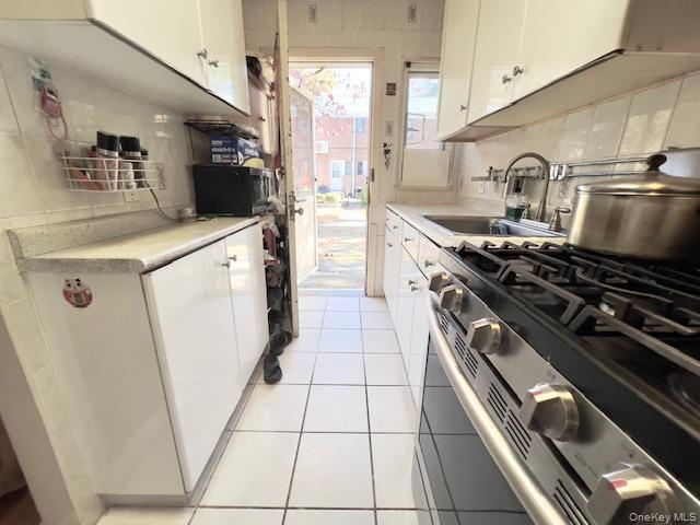 220-34 67th Avenue, Unit 2LEVELS Queens, NY 11364 - Photo 7 of 30 Kitchen featuring stainless steel gas stove, tasteful backsplash, light countertops, white cabinetry, and light tile patterned floors. to backyard .