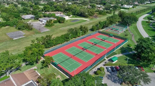 an aerial view of a tennis ground and a cars park side of the road