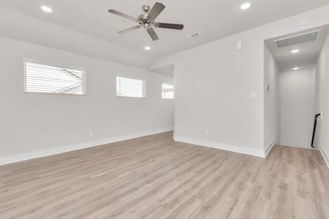 an empty room with wooden floor fan and windows
