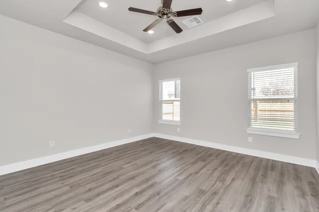 an empty room with wooden floor fan and windows