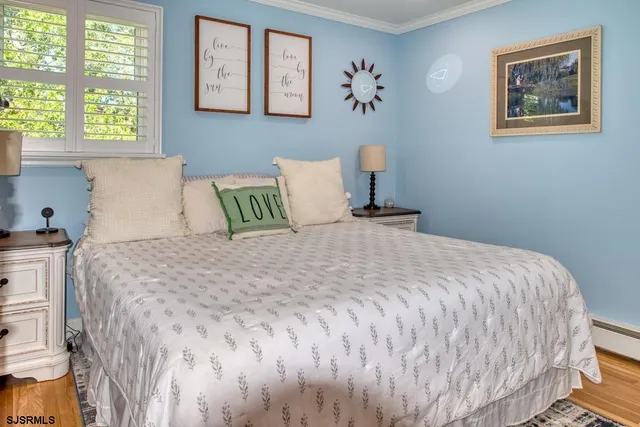 a bedroom with a bed and a lamp on dresser with wooden floor
