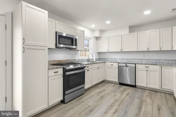 a kitchen with stainless steel appliances granite countertop a stove top oven a sink and white cabinets