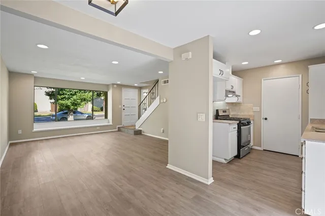 a view of an empty room with wooden floor and a kitchen