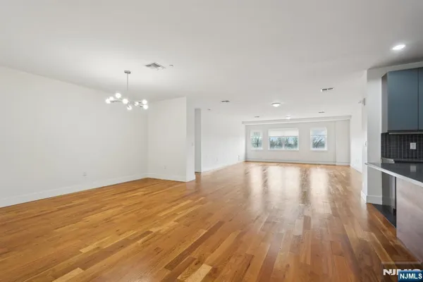 a view of an empty room with wooden floor and a kitchen