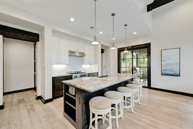 a kitchen with stainless steel appliances granite countertop a stove a refrigerator a sink a dining table and chairs with wooden floor