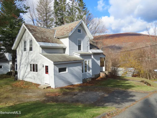 a view of a white house next to a yard with big trees