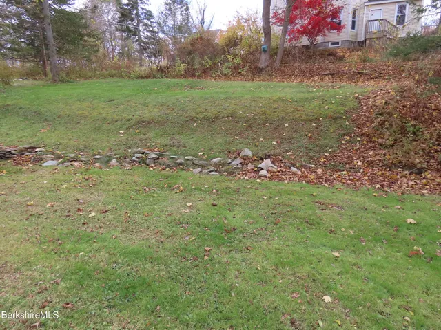 a view of a white house next to a yard with big trees