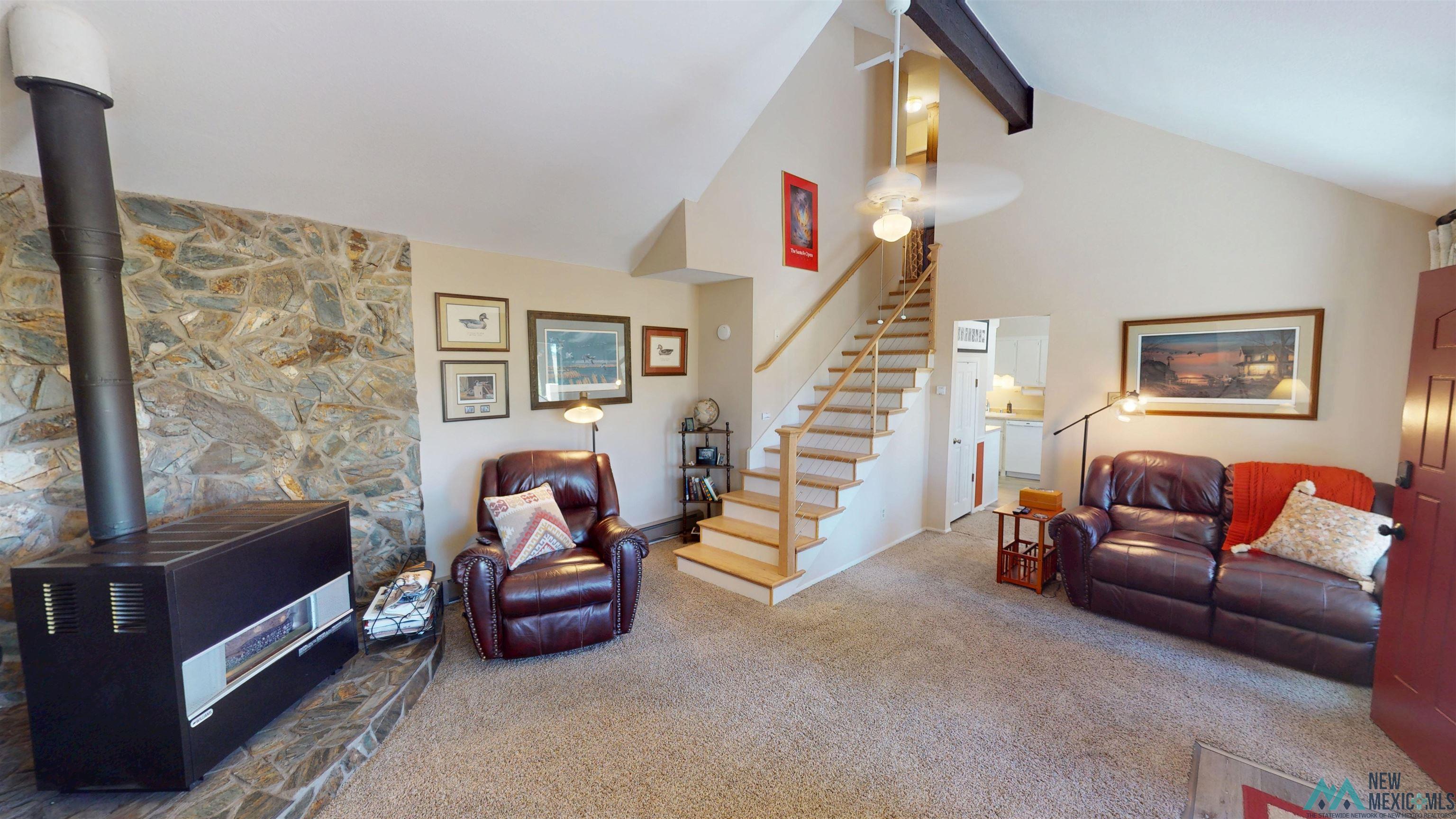 23 Pendaries Lane Rociada, NM 87742 - Photo 4 of 26 Vaulted ceiling living area featuring a stone accent wall, wood stove, carpet flooring, a wood staircase, and a ceiling fan with light fixture
