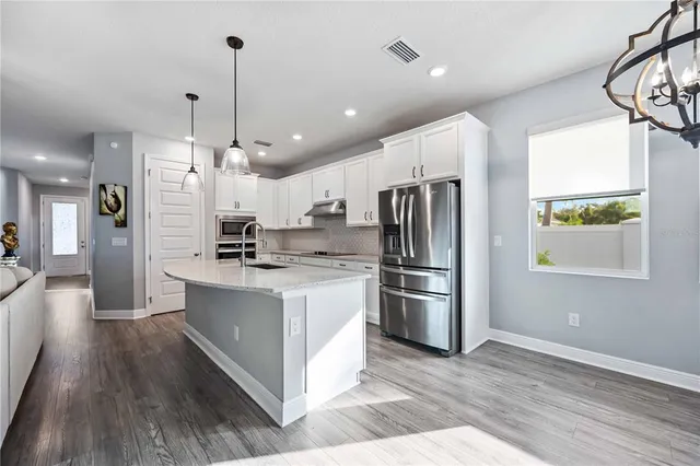 a kitchen with stainless steel appliances granite countertop a refrigerator a sink a stove and a wooden floors