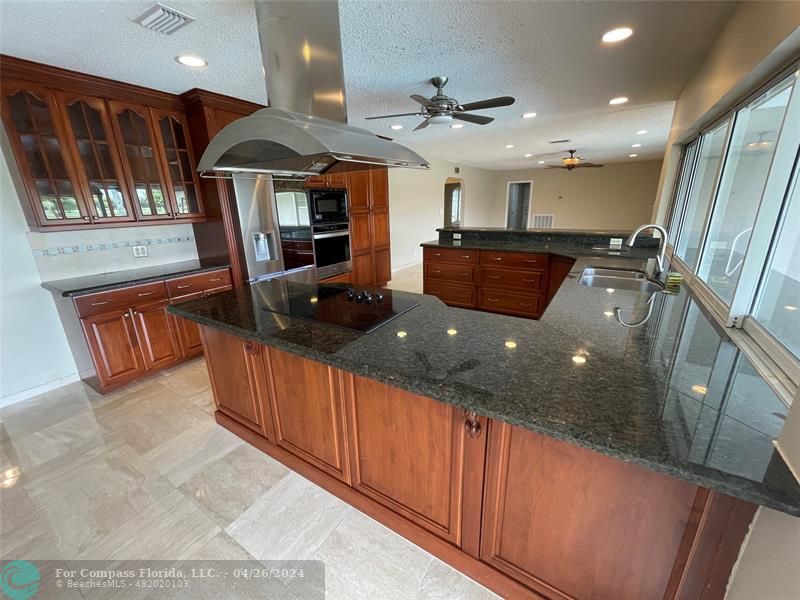 a open kitchen with stainless steel appliances granite countertop a refrigerator a oven and a sink with large countertops