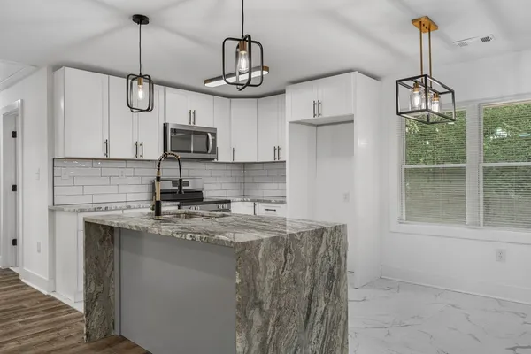 a kitchen with stainless steel appliances granite countertop cabinets a sink a window and a wooden floor