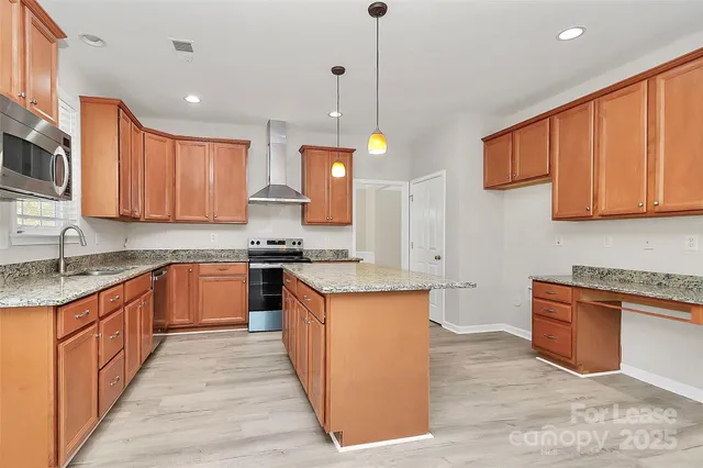 a kitchen with stainless steel appliances granite countertop wooden cabinets a sink a stove a refrigerator and island with wooden floor