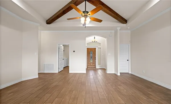 a view of an empty room and kitchen view with wooden floor