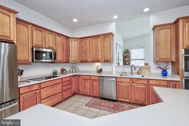 a kitchen with stainless steel appliances granite countertop wooden cabinets a sink a stove a refrigerator and dishwasher with wooden floor