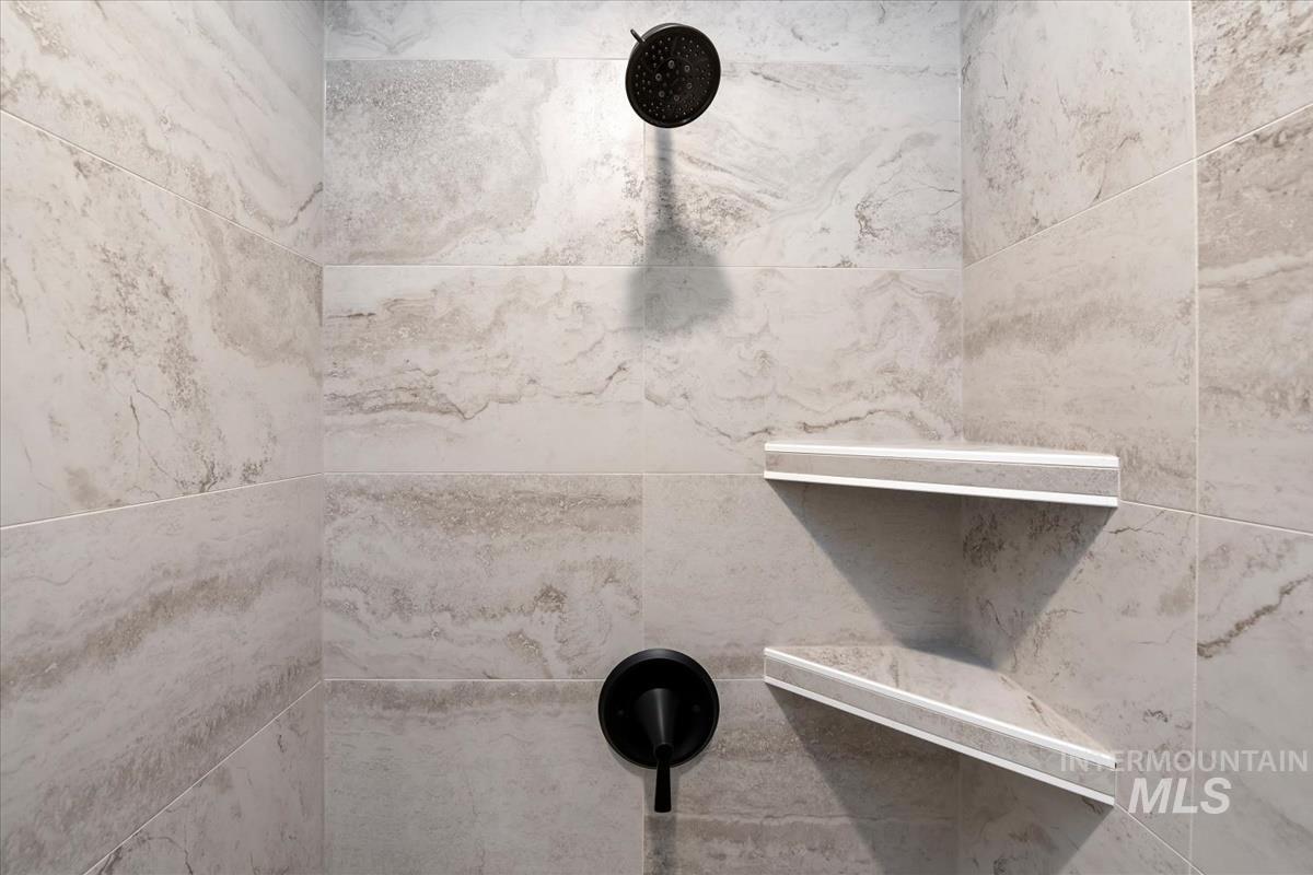 768 South Calhoun Lane Star, ID 83669 - Photo 25 of 36 Shower enclosure featuring large format stone-look tile, matte black showerhead, coordinating matte black single-handle valve trim, and two built-in corner shelves