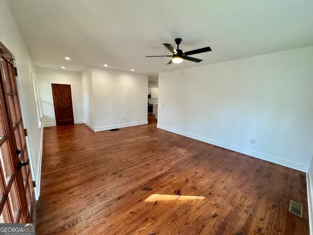 an empty room with wooden floor fan and windows