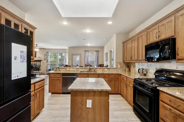 a large kitchen with stainless steel appliances granite countertop a stove top oven a sink dishwasher a refrigerator and a dining table with wooden floor