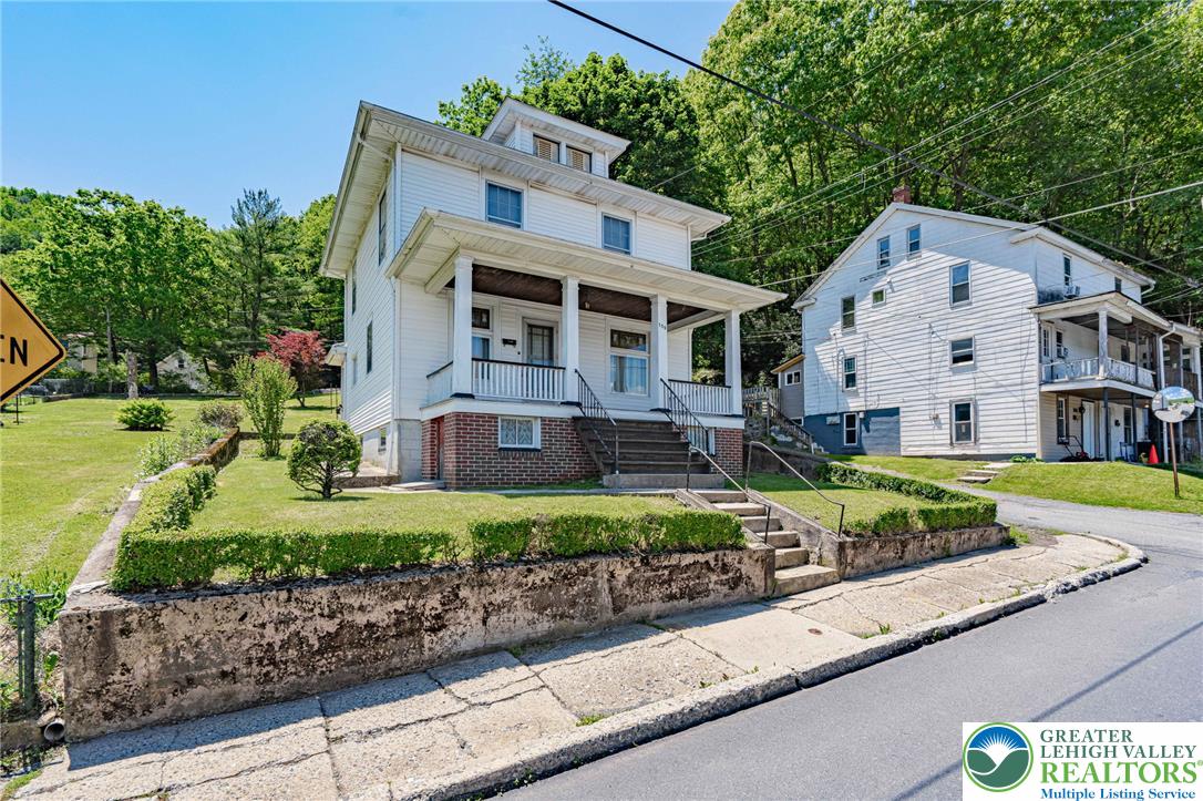 159 West Ridge Street Nesquehoning, PA 18240 - Photo 2 of 55 A charming residence with a welcoming front porch awaits, nestled against a verdant, tree-lined hillside.
