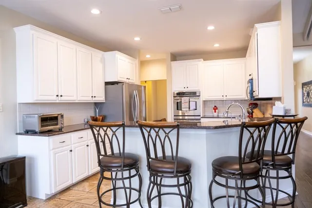 a kitchen with stainless steel appliances kitchen island granite countertop a table chairs in it and white cabinets