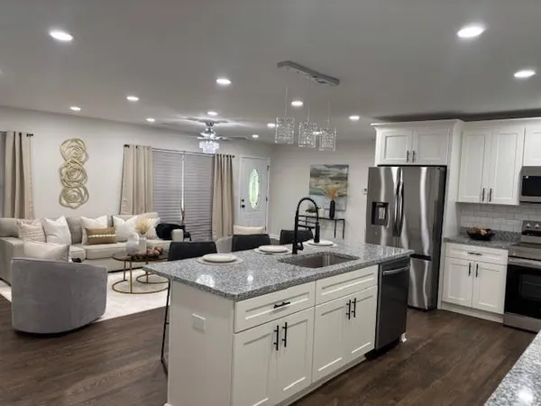 a kitchen with stainless steel appliances granite countertop a sink dishwasher a refrigerator and white cabinets with wooden floor