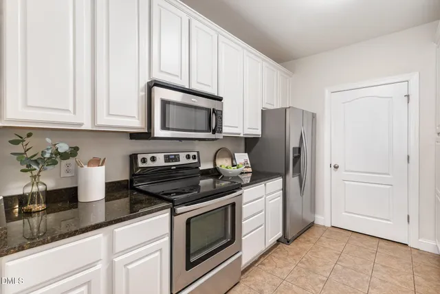 a kitchen with stainless steel appliances granite countertop white cabinets a refrigerator a stove a sink and dishwasher with wooden floor