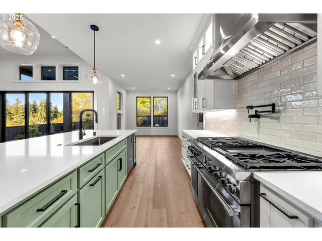 a kitchen with stainless steel appliances granite countertop a stove a sink dishwasher and white cabinets with wooden floor