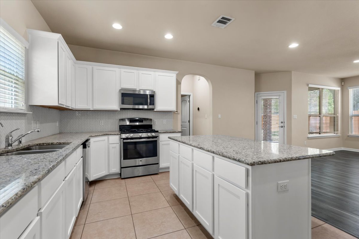 3451 Mayfield Ranch Boulevard, Unit 311 Round Rock, TX 78681 - Photo 13 of 40 Kitchen featuring white cabinetry, granite countertops, stainless steel appliances, and a mosaic tile backsplash