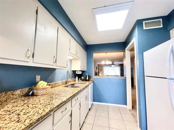 a kitchen with granite countertop a refrigerator a sink and white cabinets