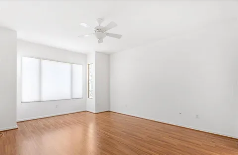 an empty room with wooden floor fan and windows