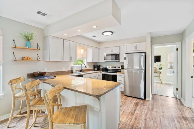 a kitchen with stainless steel appliances granite countertop a refrigerator a stove top oven a sink dishwasher and white cabinets with wooden floor