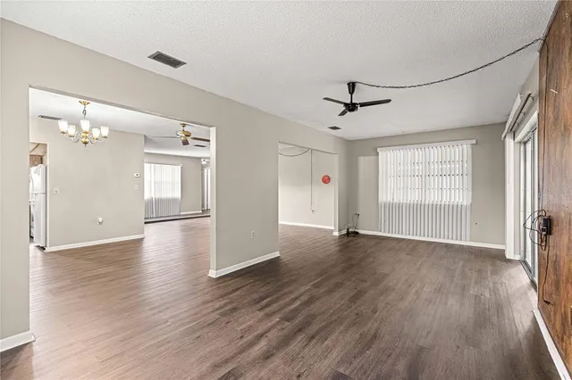 an empty room with wooden floor chandelier and windows