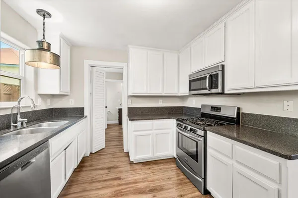 a kitchen with stainless steel appliances granite countertop white cabinets a sink a stove a microwave and wooden floors